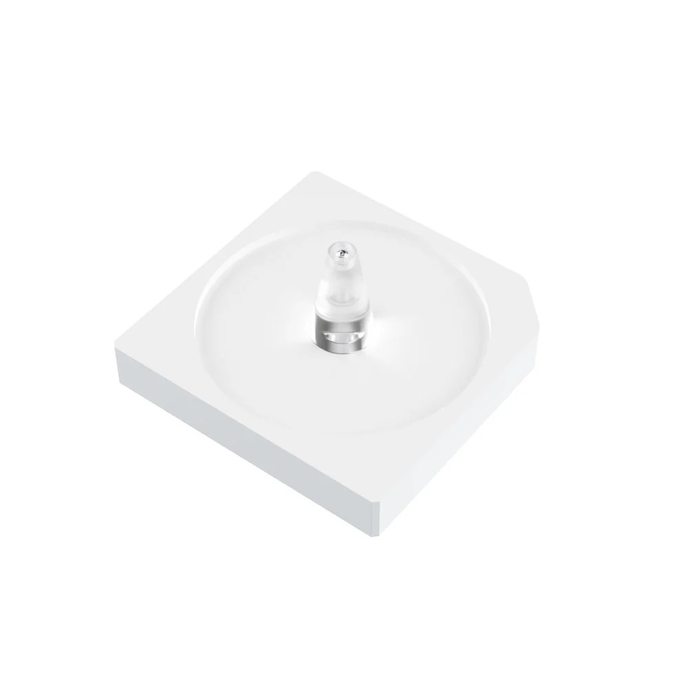A square plastic device with a circle engraved in the centre, one bevelled edge and a transparent plastic cone in the middle with a small metal ball embedded at the top.